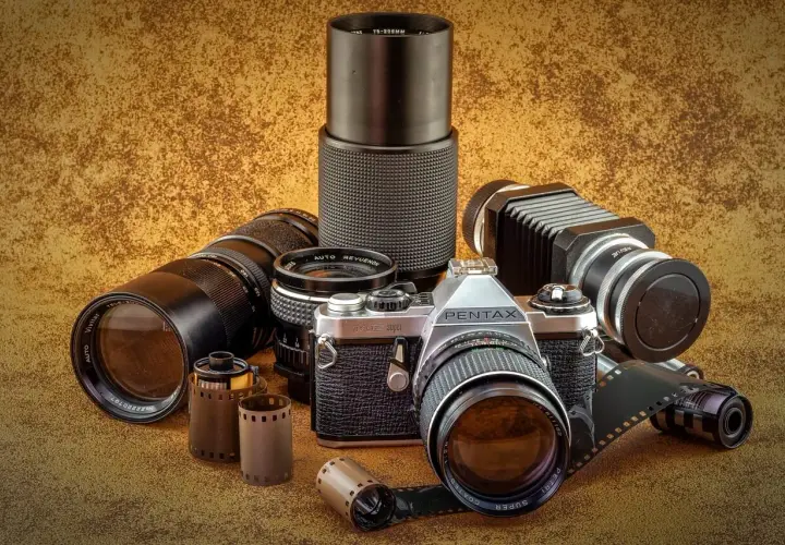 Zestaw fotograficzny: aparat Pentax JMC Super, obiektywy Vivitar i Revue, mieszek, rolki filmu. Klasyczny rodzaj aparatu fotograficznego.