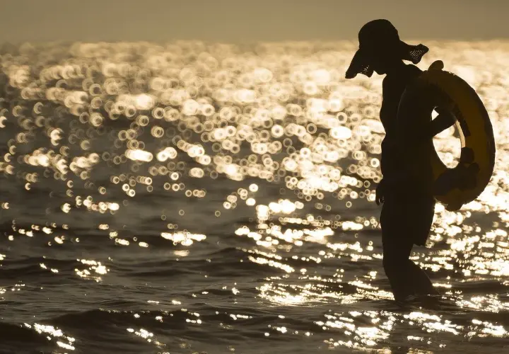Sylwetka w kapeluszu z kołem ratunkowym na plaży. Piękna, złota bokeh fotografia falującego morza o zachodzie słońca.
