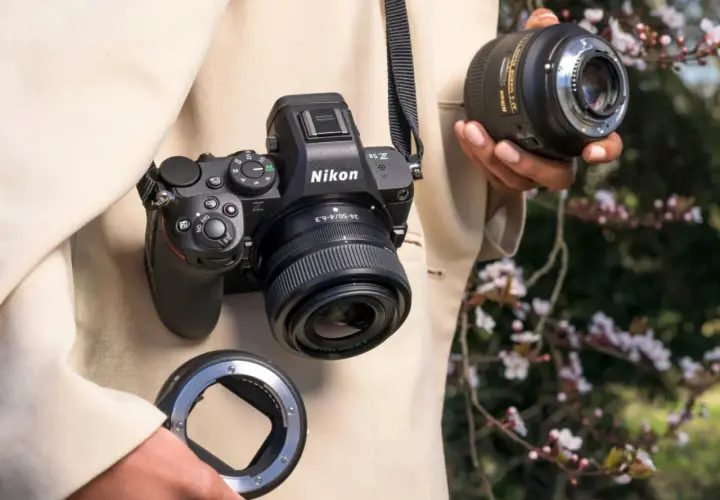 Osoba trzyma aparat Nikon Z5II z obiektywem i adapterem. W tle kwitnące drzewa.