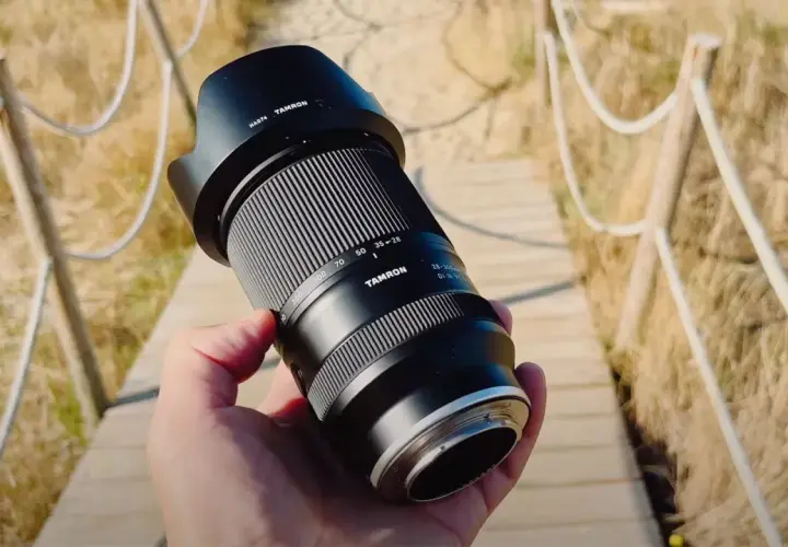 Dłoń trzyma obiektyw Tamron 28-300mm, gotowy do uchwycenia odległych detali. Jakie przybliżenie oferuje ten obiektyw?