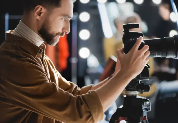 Fotograf z brodą ustawia aparat na statywie, przygotowując się do precyzyjnego pomiaru światła w studio.
