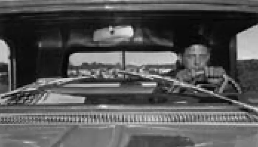 Lee Friedlander za kierownicą, patrzący przed siebie. Widok z wnętrza samochodu.