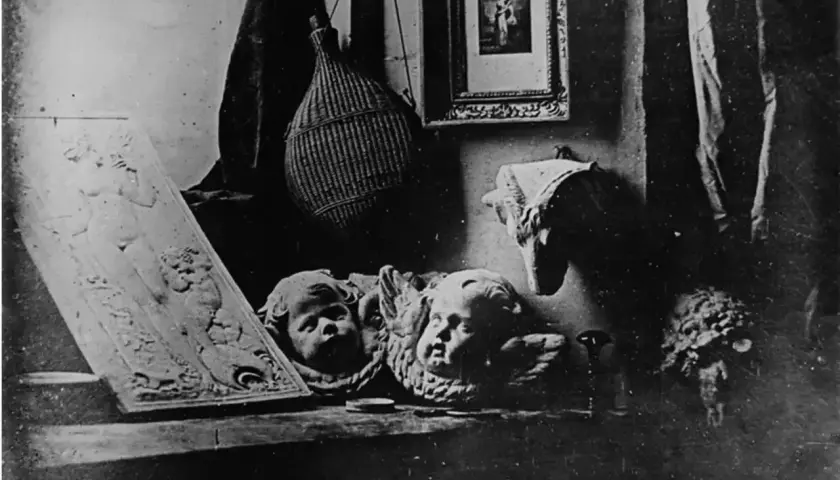Studiowe ujęcie z początków fotografii: płaskorzeźba z postacią, dwa aniołki, pleciona butla i obrazek.