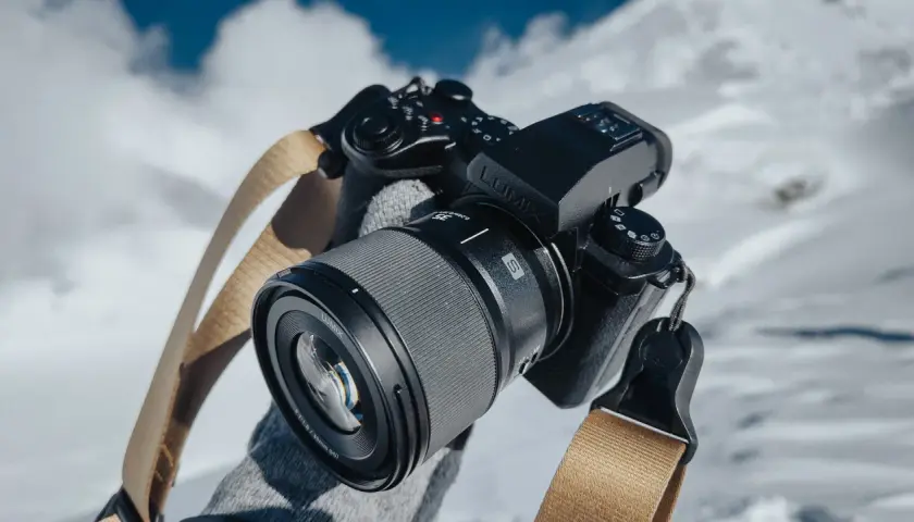 Ręce w rękawiczkach trzymają aparat Lumix z obiektywem, gotowe do uchwycenia zimowych krajobrazów.