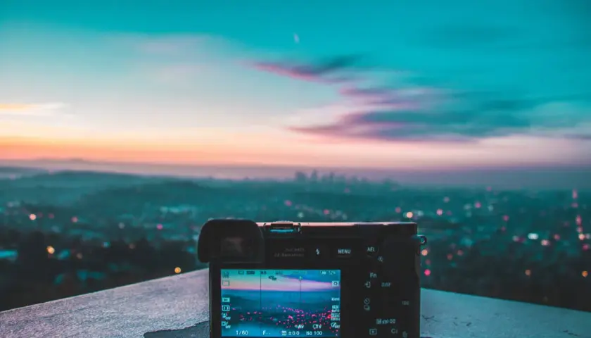 Aparat fotograficzny na tle miasta o zachodzie słońca. Na ekranie widać rozmyte światła miasta i niebo, tworzące piękne smugi światła na zdjęciach.