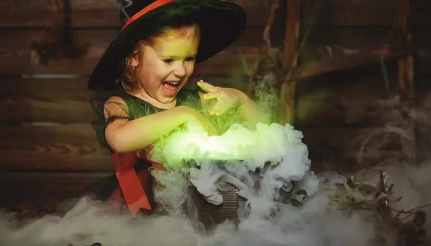 Mała czarownica w kapeluszu miesza w kociołku, tworząc zielony dym. To jak zrobic dym na Halloween!