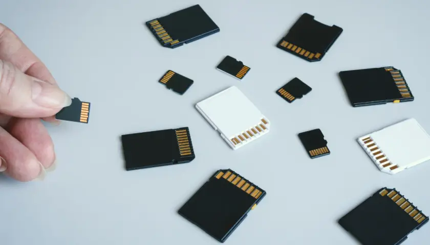 Różne rodzaje kart pamięci: microSD, SD i adaptery. Dłoń trzyma małą kartę microSD, obok leżą inne karty.