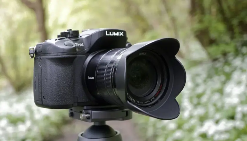 Czarny aparat Panasonic Lumix GH4 z obiektywem na statywie, w tle zielony las.