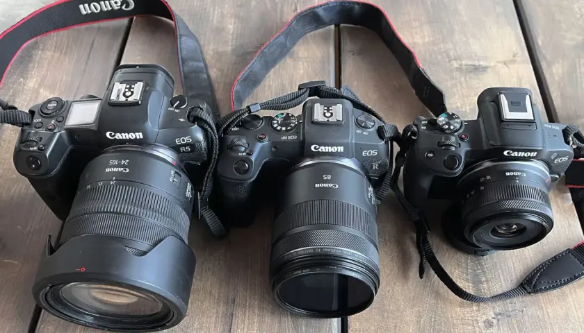 Trzy aparaty Canon EOS: R5 z obiektywem 24-105mm, RP z 85mm i R50 z 18-45mm. Różne obiektywy, od szerokokątnych po tele, pokazują wszechstronność systemu.