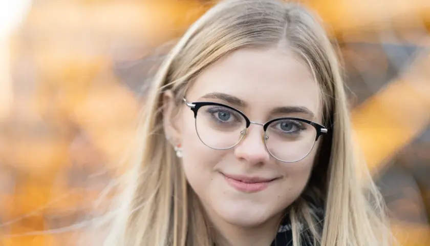 Uśmiechnięta blondynka w okularach, z rozmyciem tła. Idealna ogniskowa do portretu, by podkreślić oczy.