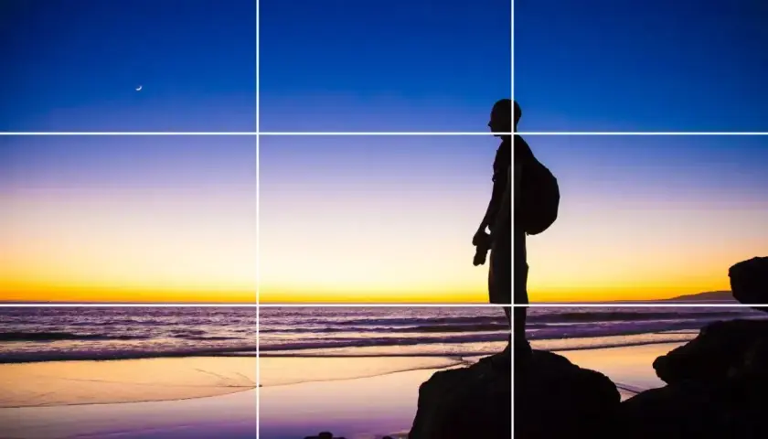 Sylwetka fotografa na plaży o zachodzie słońca, z księżycem na niebie. Kompozycja wykorzystuje trójpodział w fotografii.