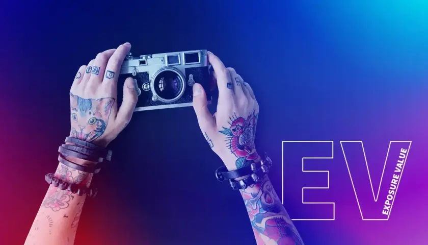 Dłonie z tatuażami trzymają aparat. To co to jest fotografia, uchwycone w kadrze z napisem EV.