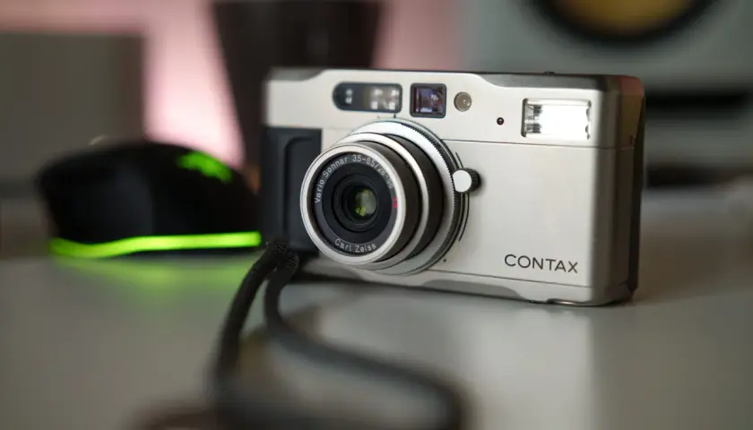 Srebrny aparat Contax TVS z obiektywem Carl Zeiss Vario-Sonnar. Obok widoczna jest czarna myszka z zielonym podświetleniem.