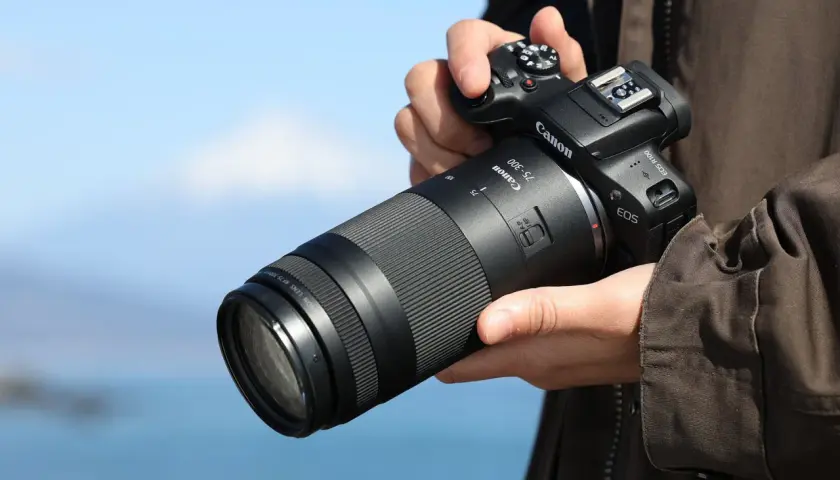 Dłoń trzyma aparat Canon z obiektywem 75-300, idealnym do fotografii przyrodniczej i sportowej, pozwalającym uchwycić odległe detale.