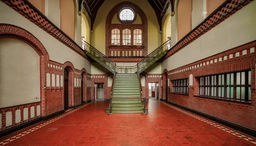 Imponująca klatka schodowa w zabytkowym budynku. Fotografia architektury z czerwonej cegły, zielonymi stopniami i ozdobnymi balustradami.