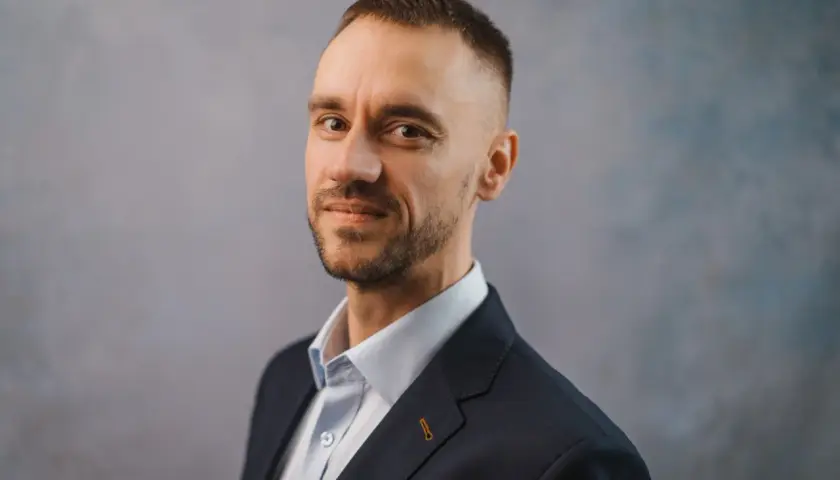 Portret Michała Wilczewskiego w ciemnej marynarce i jasnej koszuli, z lekkim zarostem i krótką fryzurą.
