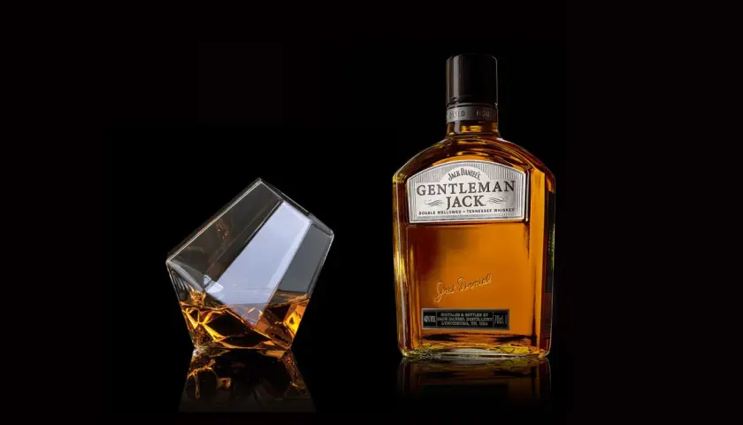 Elegancka butelka Gentleman Jack i szklanka z bursztynowym trunkiem. Stylowe zdjecia produktowe.