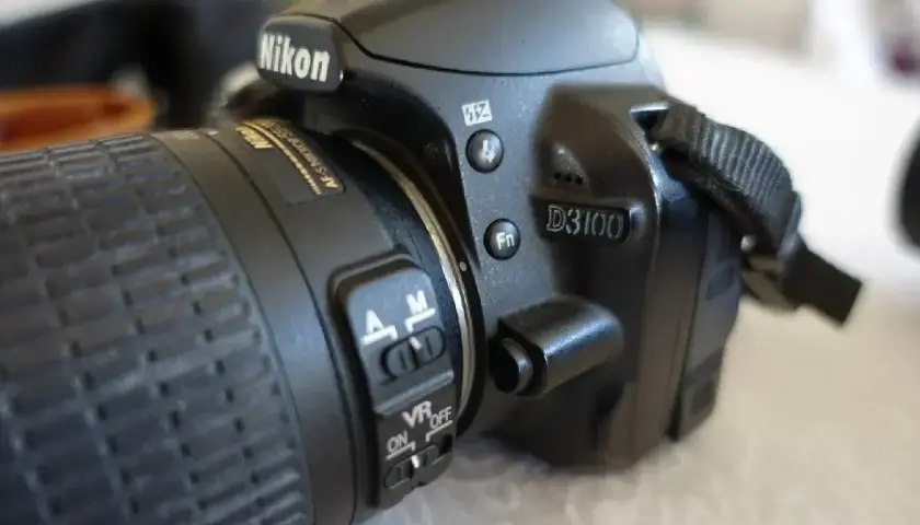 Zbliżenie na aparat Nikon D3100. Widoczne przyciski sterujące, przełącznik AF/M i VR ON/OFF. Idealny do poznawania nikon d3100 dane techniczne.