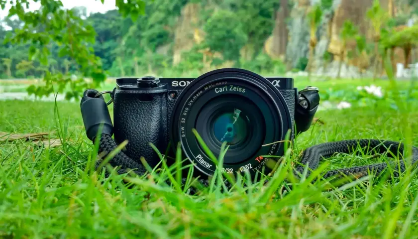 Aparat Sony z obiektywem Carl Zeiss leży na trawie. W tle skaliste wzgórza i zieleń. Idealne do fotografii przyrodniczej.