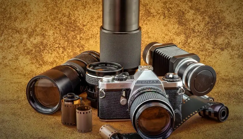 Zestaw fotograficzny: aparat Pentax JMC Super, obiektywy Vivitar i Revue, mieszek, rolki filmu. Klasyczny rodzaj aparatu fotograficznego.