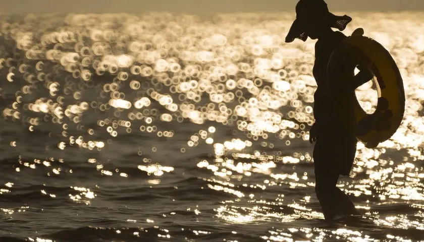 Sylwetka w kapeluszu z kołem ratunkowym na plaży. Piękna, złota bokeh fotografia falującego morza o zachodzie słońca.