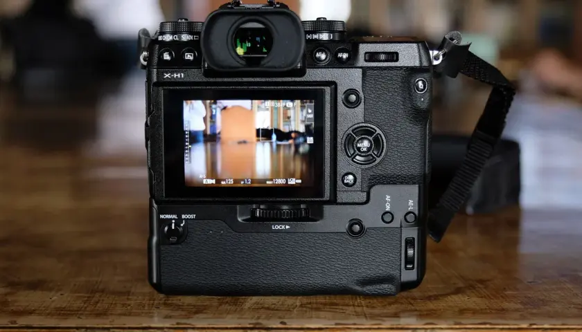 Tył aparatu Fujifilm X-H1 z widocznym ekranem LCD, przyciskami sterującymi i paskiem na nadgarstek.