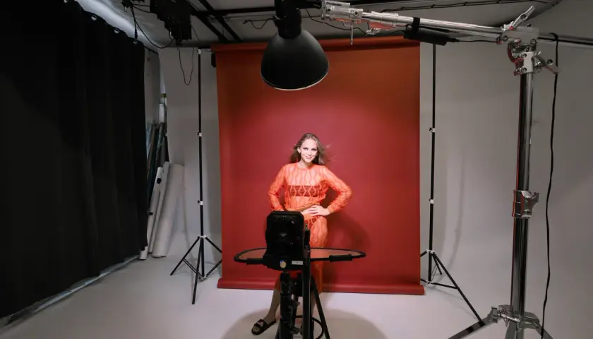 Modelka w studiu, testująca różne rodzaje oświetlenia w fotografii. Czerwone tło, lampy studyjne i sprzęt do tworzenia efektów.