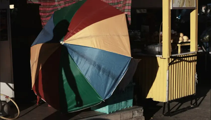 Kolorowy parasol rzuca cień na uliczny stragan z mango sticky rice. Fotografia miejska.