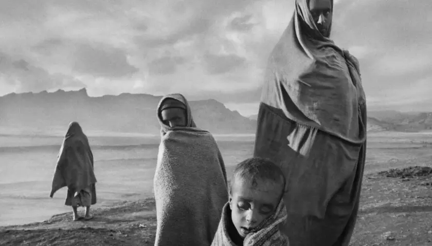 Dzieci i dorosły owinięci w tkaniny, w surowym krajobrazie. Wzrok przyciąga spojrzenie jednego z nich, uchwycone przez Sebastiao Salgado.