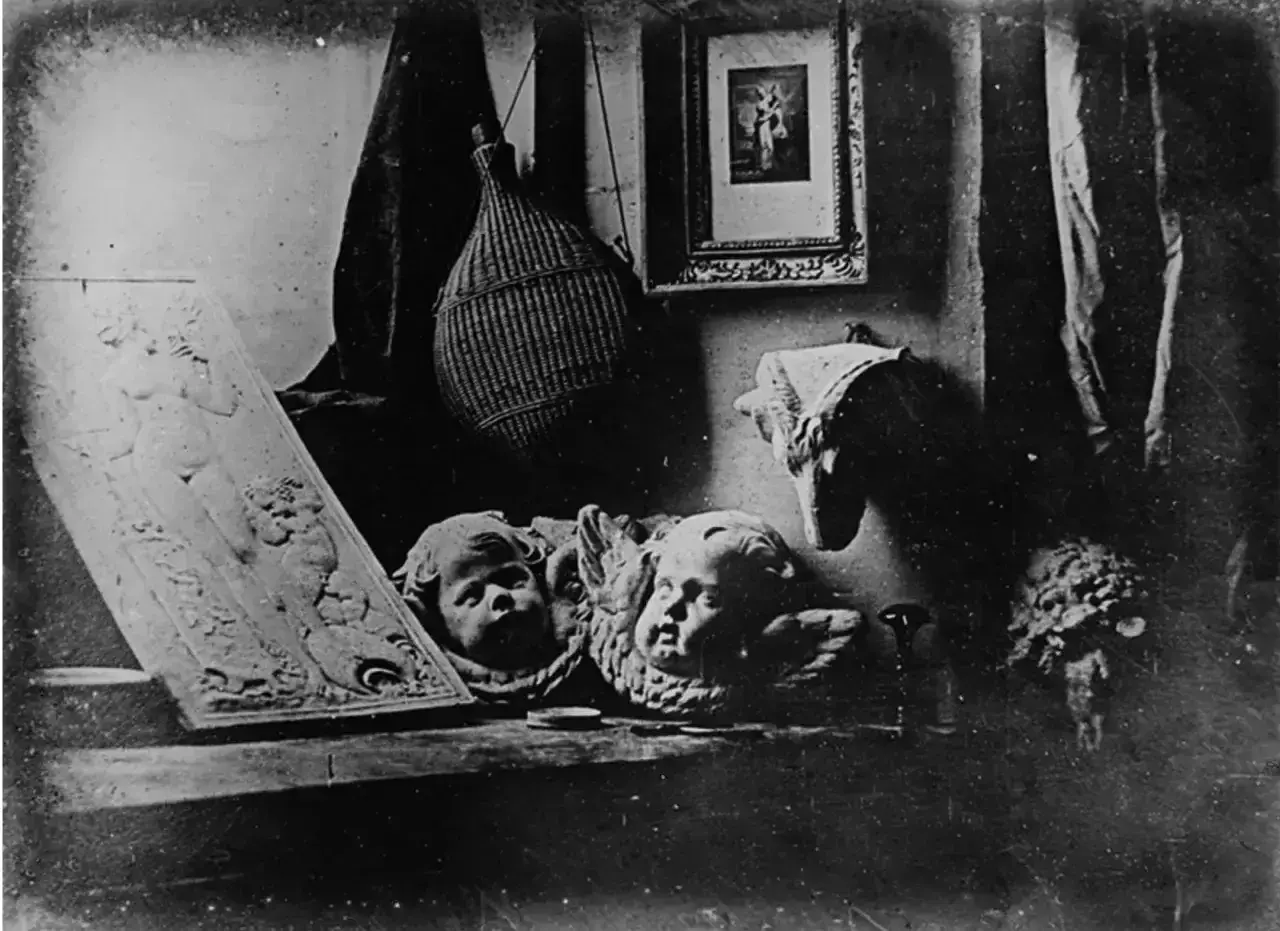 Studiowe ujęcie z początków fotografii: płaskorzeźba z postacią, dwa aniołki, pleciona butla i obrazek.