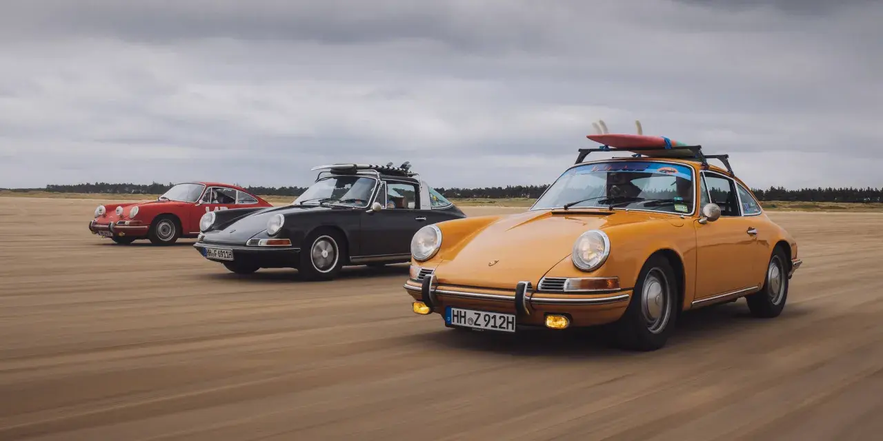 Trzy klasyczne Porsche jadące po plaży. Kompozycja dynamiczna fotografia z deskami surfingowymi na dachu.