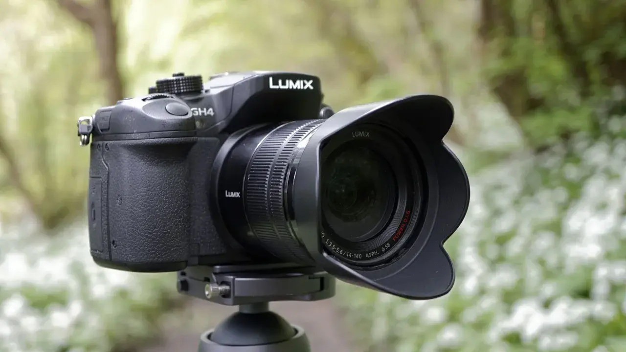 Czarny aparat Panasonic Lumix GH4 z obiektywem na statywie, w tle zielony las.