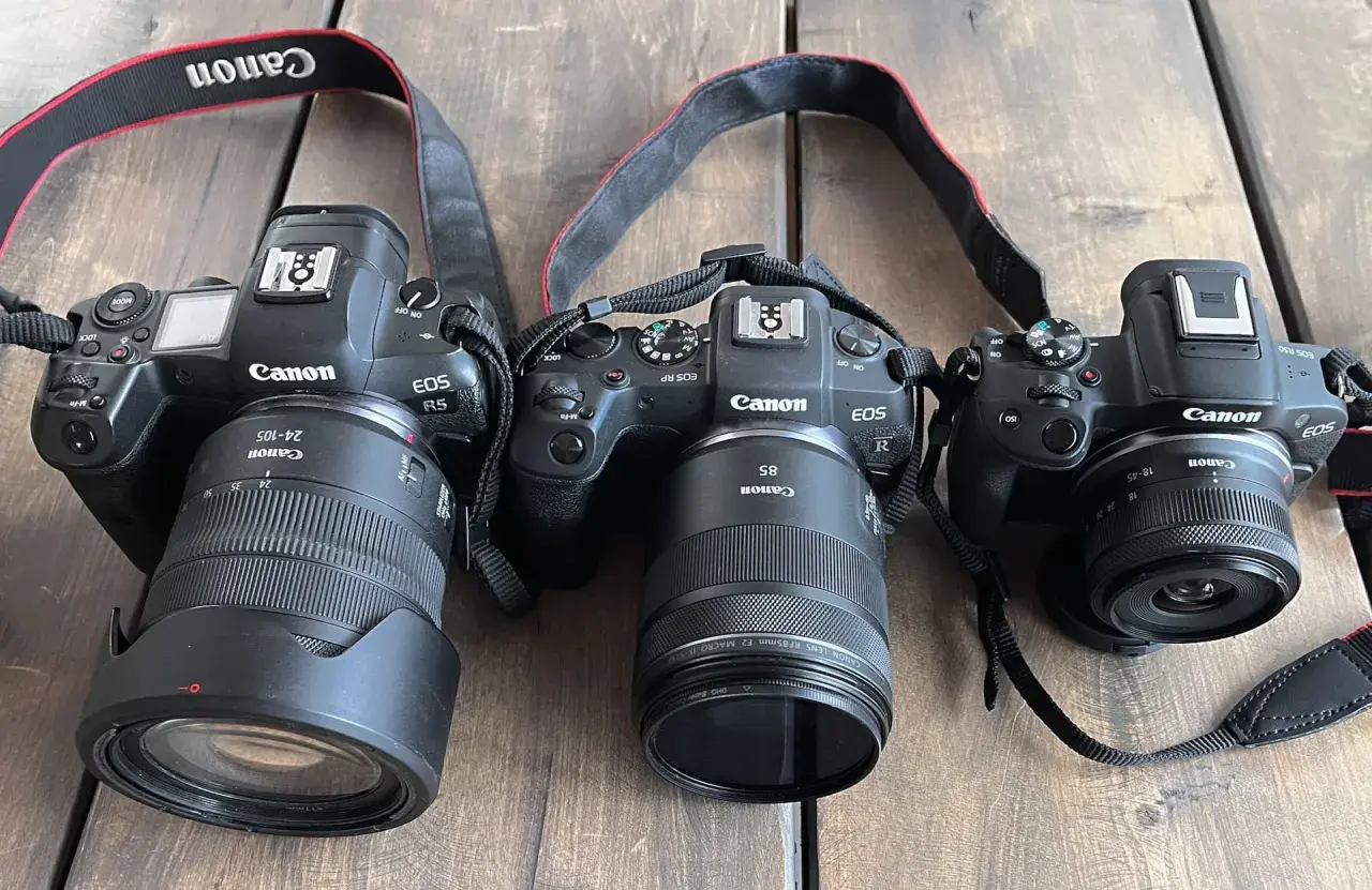 Trzy aparaty Canon EOS: R5 z obiektywem 24-105mm, RP z 85mm i R50 z 18-45mm. Różne obiektywy, od szerokokątnych po tele, pokazują wszechstronność systemu.