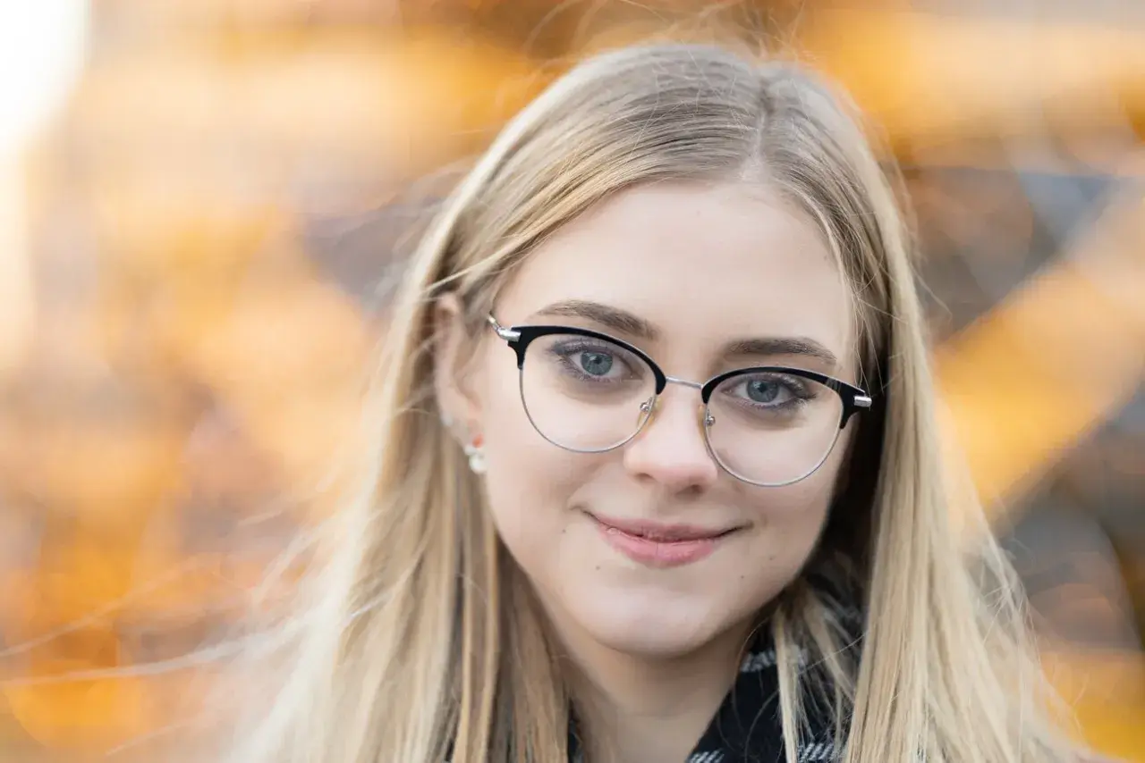 Uśmiechnięta blondynka w okularach, z rozmyciem tła. Idealna ogniskowa do portretu, by podkreślić oczy.