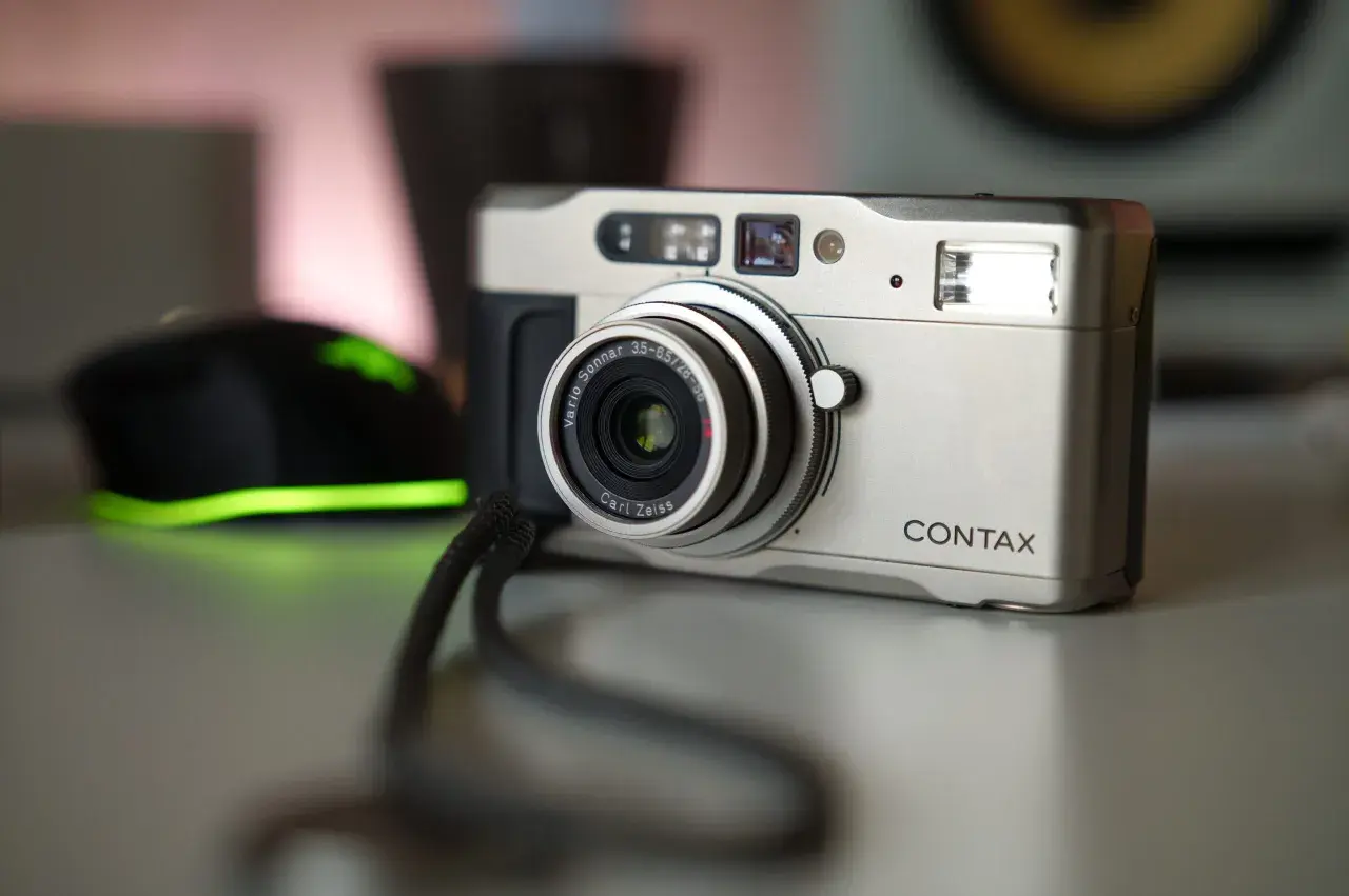 Srebrny aparat Contax TVS z obiektywem Carl Zeiss Vario-Sonnar. Obok widoczna jest czarna myszka z zielonym podświetleniem.