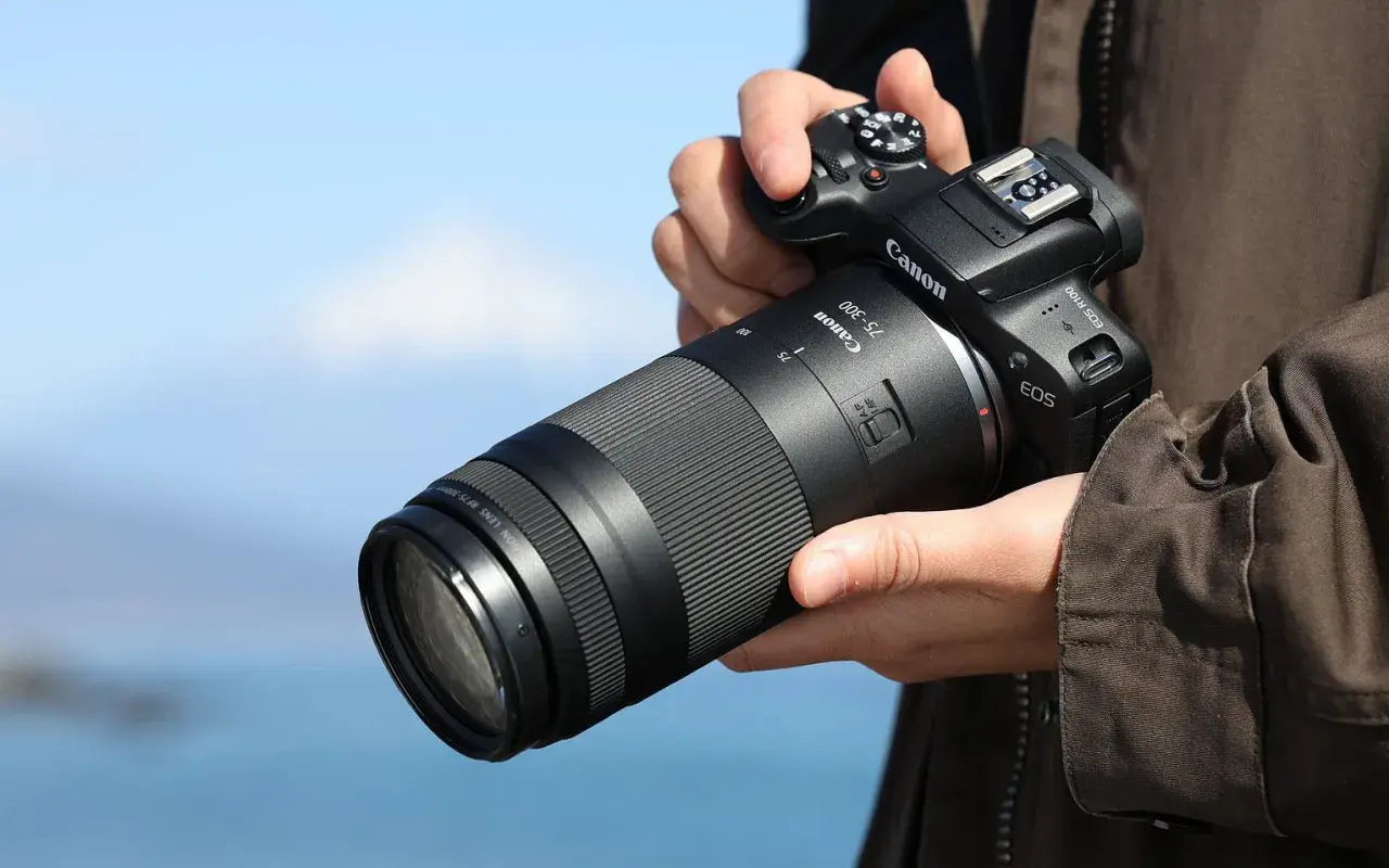 Dłoń trzyma aparat Canon z obiektywem 75-300, idealnym do fotografii przyrodniczej i sportowej, pozwalającym uchwycić odległe detale.