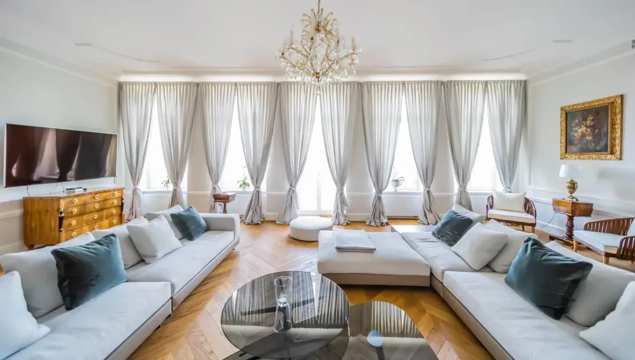 Eleganckie zdjecia wnetrz: przestronny salon z białymi sofami, kryształowym żyrandolem i zasłonami.