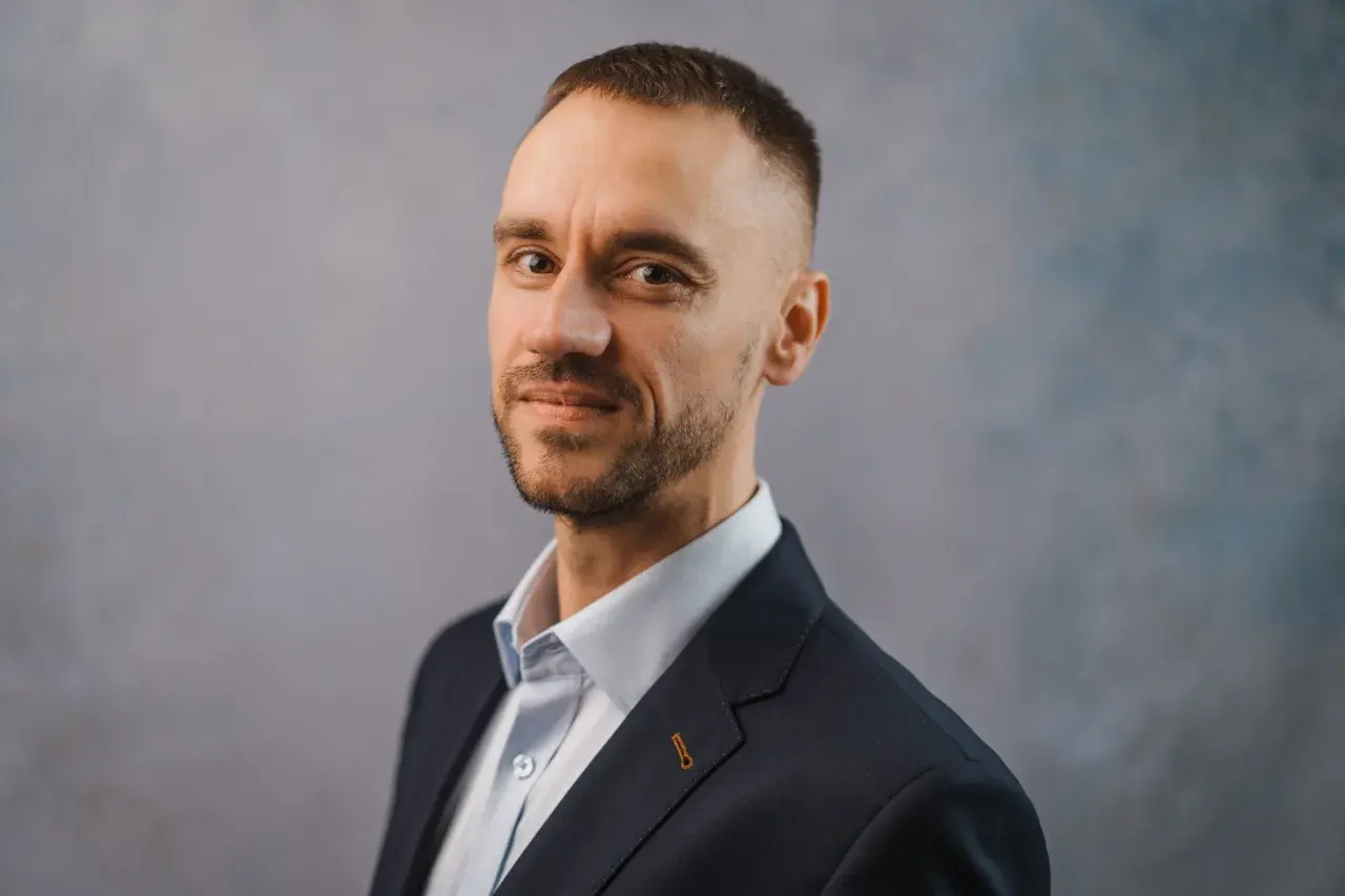 Portret Michała Wilczewskiego w ciemnej marynarce i jasnej koszuli, z lekkim zarostem i krótką fryzurą.
