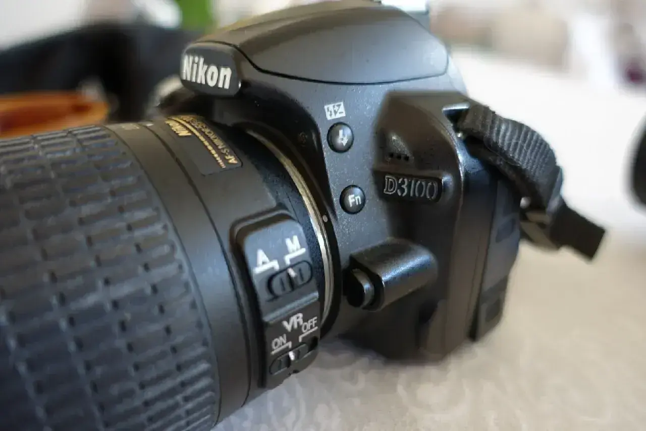 Zbliżenie na aparat Nikon D3100. Widoczne przyciski sterujące, przełącznik AF/M i VR ON/OFF. Idealny do poznawania nikon d3100 dane techniczne.
