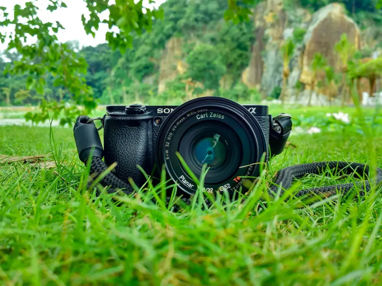Aparat Sony z obiektywem Carl Zeiss leży na trawie. W tle skaliste wzgórza i zieleń. Idealne do fotografii przyrodniczej.