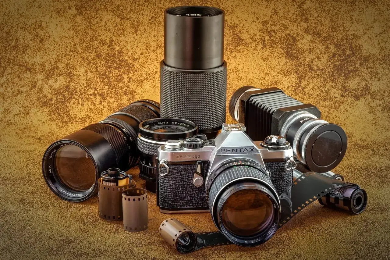 Zestaw fotograficzny: aparat Pentax JMC Super, obiektywy Vivitar i Revue, mieszek, rolki filmu. Klasyczny rodzaj aparatu fotograficznego.