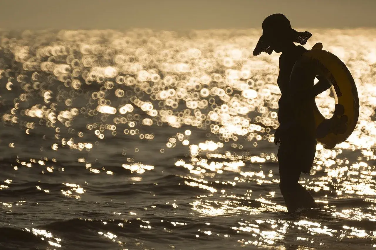 Sylwetka w kapeluszu z kołem ratunkowym na plaży. Piękna, złota bokeh fotografia falującego morza o zachodzie słońca.