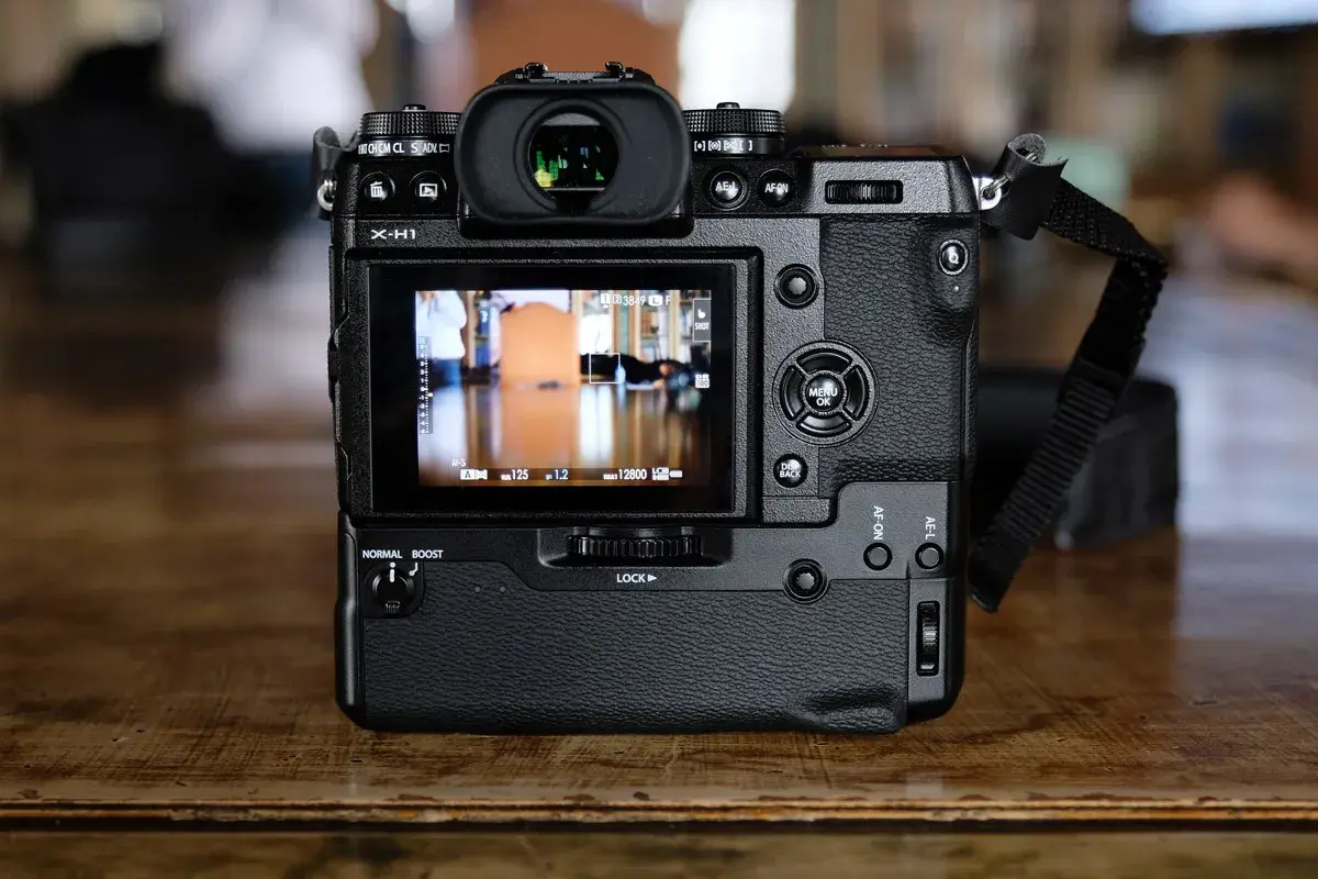 Tył aparatu Fujifilm X-H1 z widocznym ekranem LCD, przyciskami sterującymi i paskiem na nadgarstek.