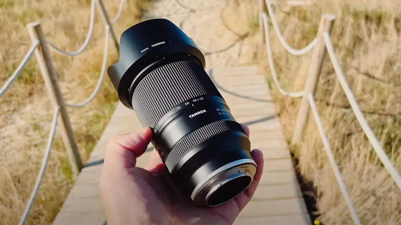 Dłoń trzyma obiektyw Tamron 28-300mm, gotowy do uchwycenia odległych detali. Jakie przybliżenie oferuje ten obiektyw?