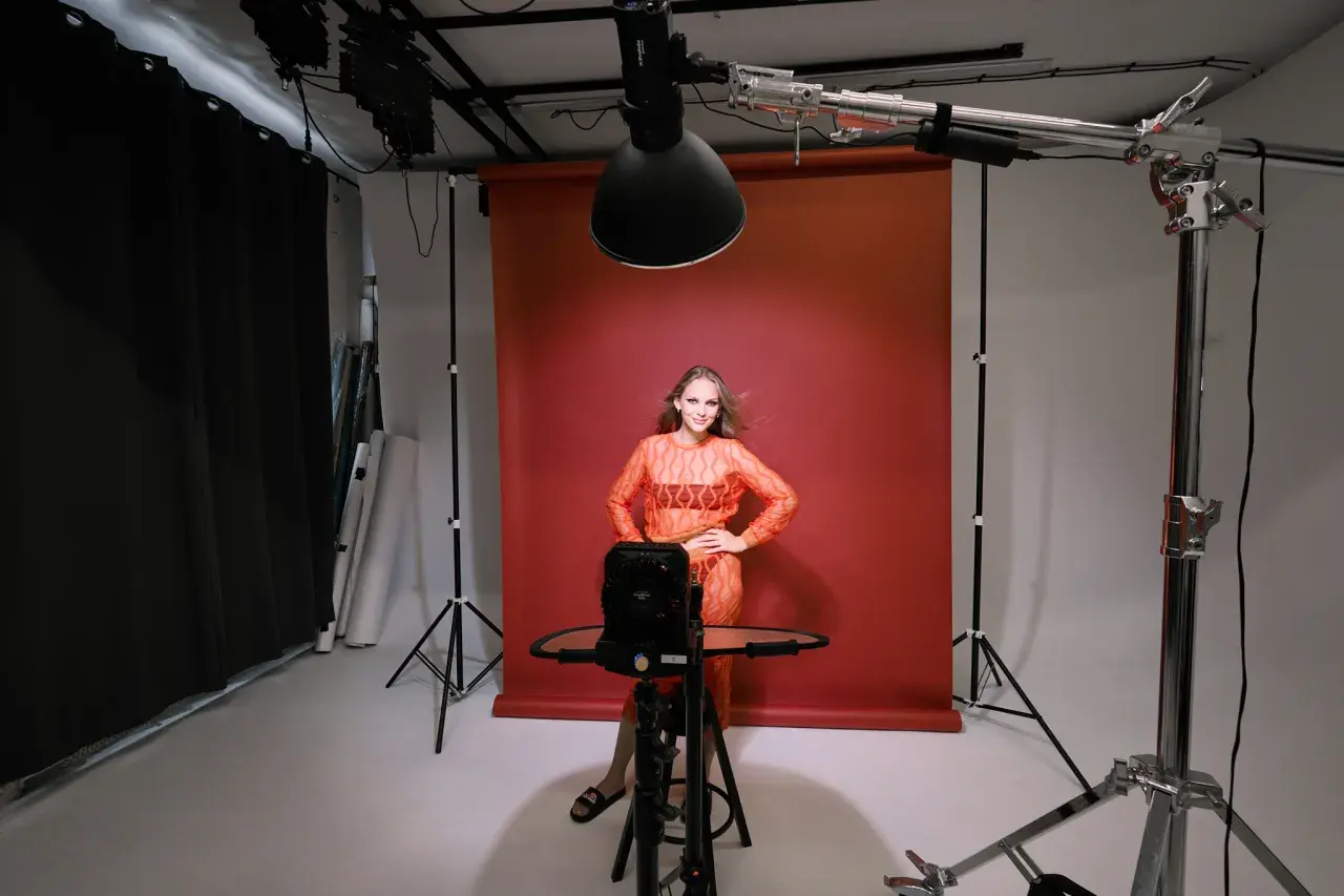 Modelka w studiu, testująca różne rodzaje oświetlenia w fotografii. Czerwone tło, lampy studyjne i sprzęt do tworzenia efektów.