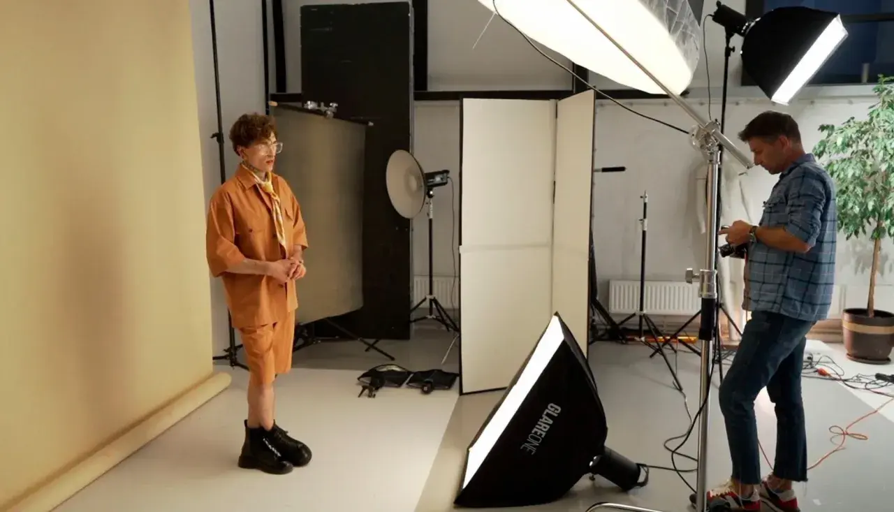 Sesja zdjęciowa w studiu. Model w pomarańczowym stroju pozuje, fotograf z aparatem sprawdza ujęcia. To właśnie jest tethering – podgląd zdjęć na żywo.