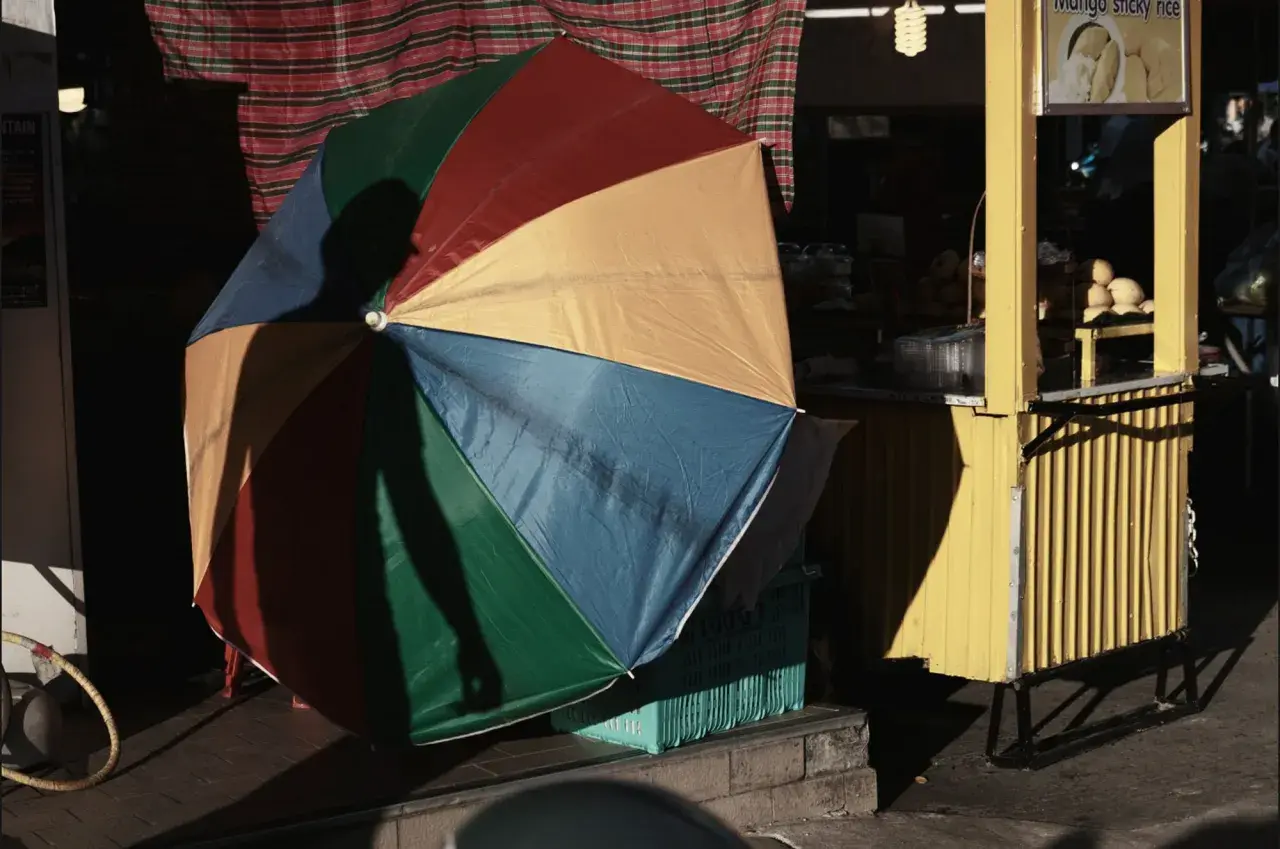 Kolorowy parasol rzuca cień na uliczny stragan z mango sticky rice. Fotografia miejska.