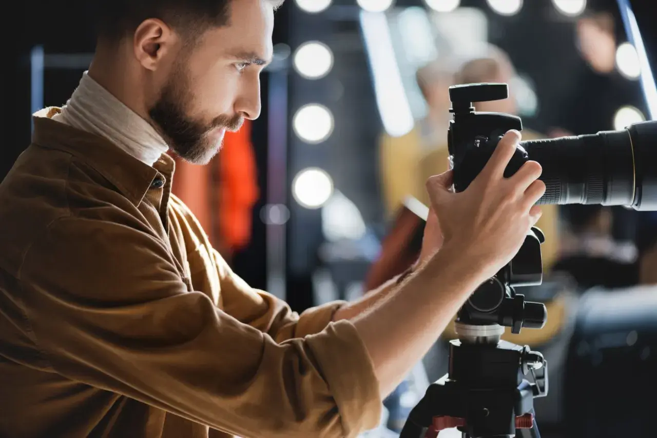 Fotograf z brodą ustawia aparat na statywie, przygotowując się do precyzyjnego pomiaru światła w studio.