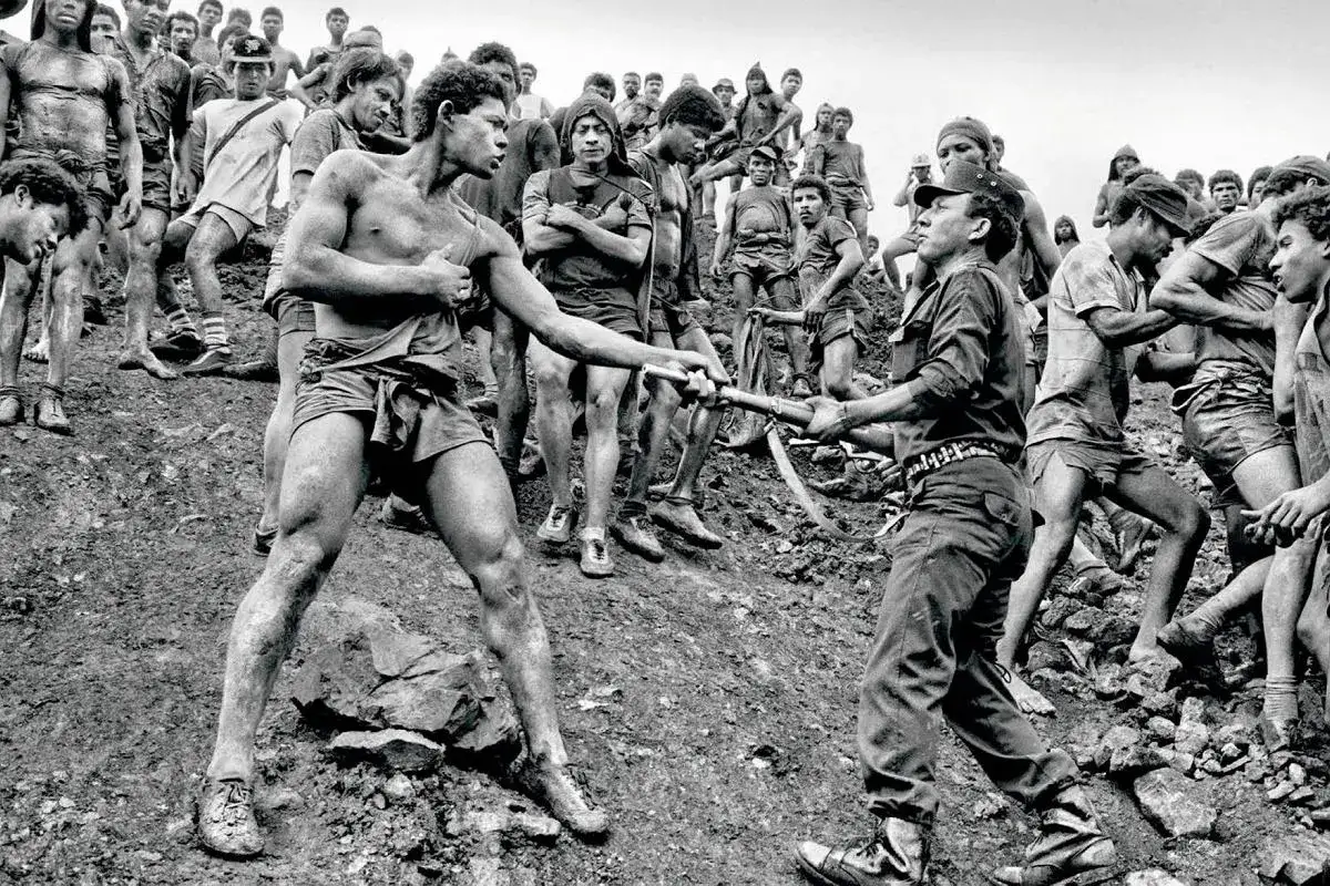 Sebastiao Salgado uchwycił moment, gdy dwaj mężczyźni w kopalni złota wymieniają się narzędziami. Wokół nich tłum innych górników.