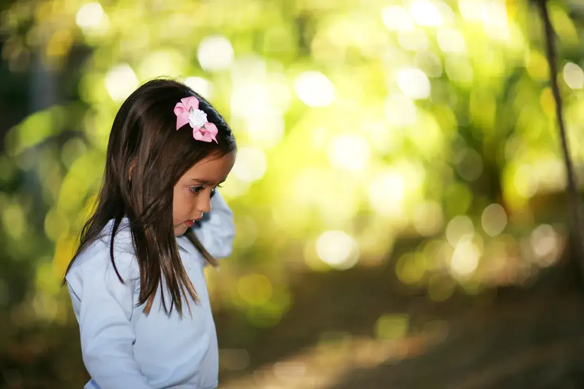 Mała dziewczynka z r&oacute;żową kokardką na głowie, wpatrzona w bok. Piękna bokeh fotografia.